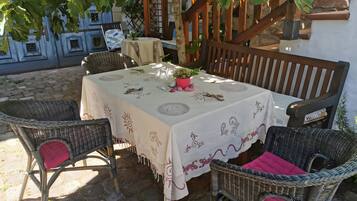 Een overdekt terras met rieten stoelen, een tafel met wit tafelkleed en een trap op de achtergrond.