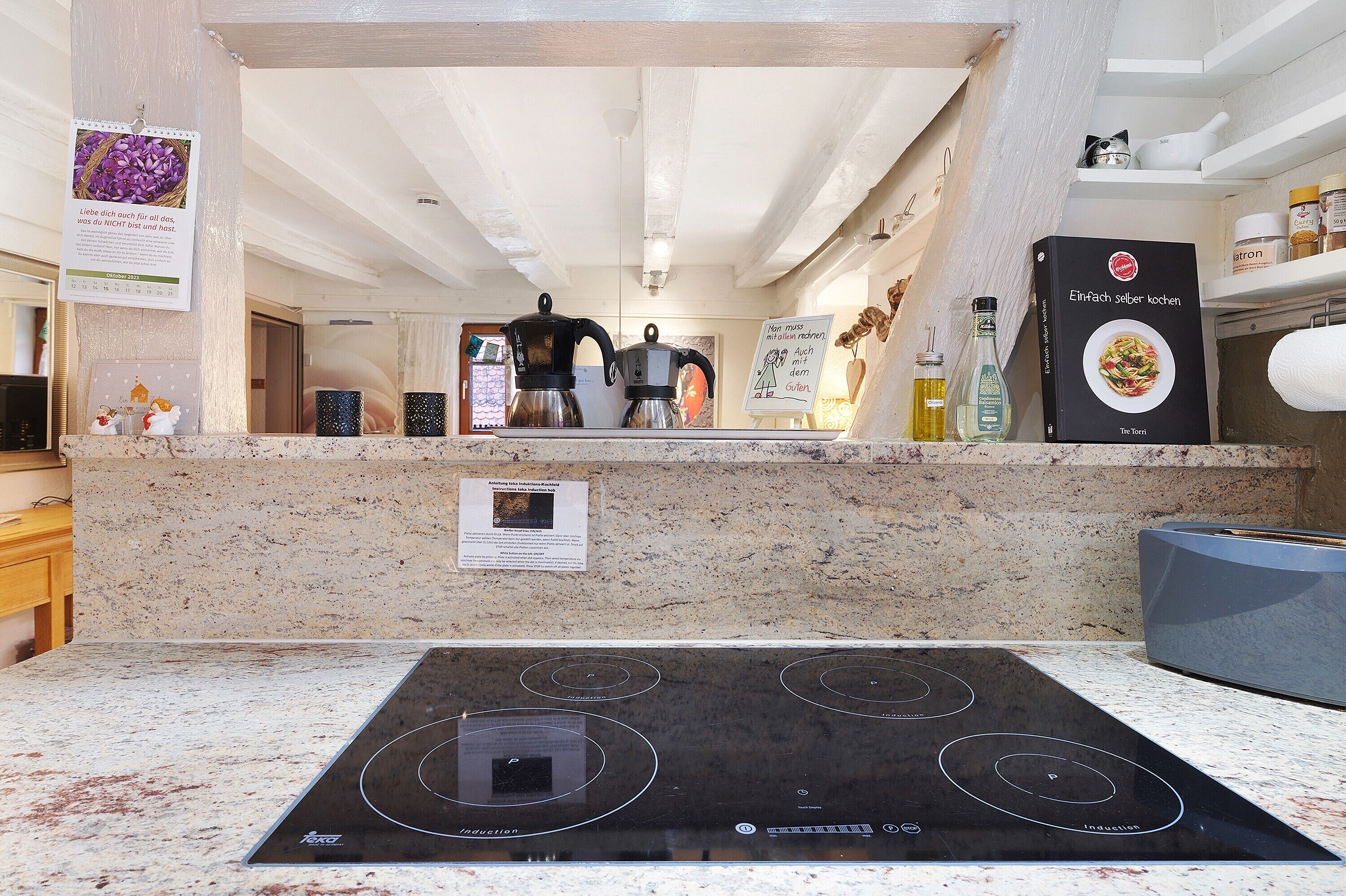 Une cuisine dotée d’une plaque de cuisson à induction noire, d’un plan de travail en granit et d’une machine à café.