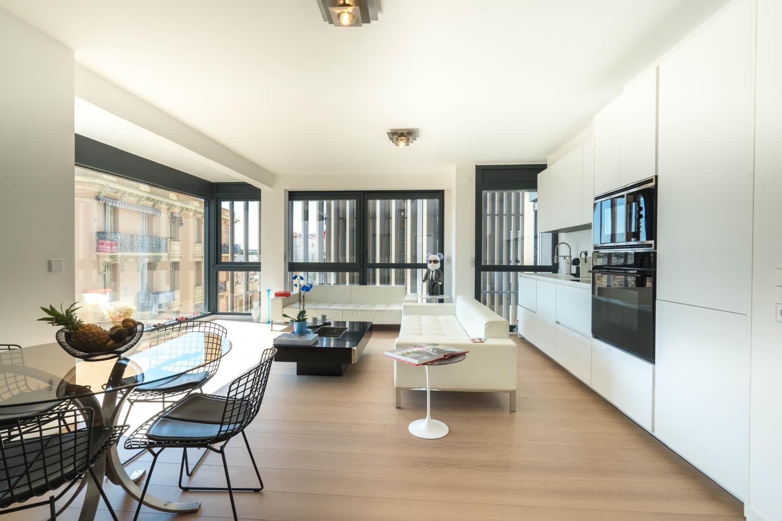 A modern kitchen with white cabinets, a black oven, and a dining area with a glass table and chairs.