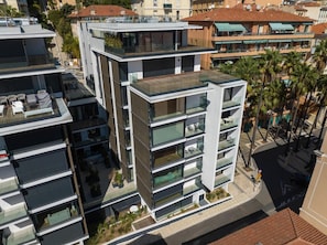 A multi-story residential building with balconies, a rooftop terrace, and a street view with palm trees.