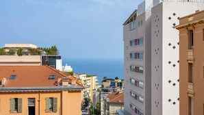 A coastal cityscape with a mix of modern and traditional architecture, including a building with a red-tiled roof and another with a white facade and decorative elements. - Appartement de Luxe 3BR vue  sur la Mer (Beausoleil)