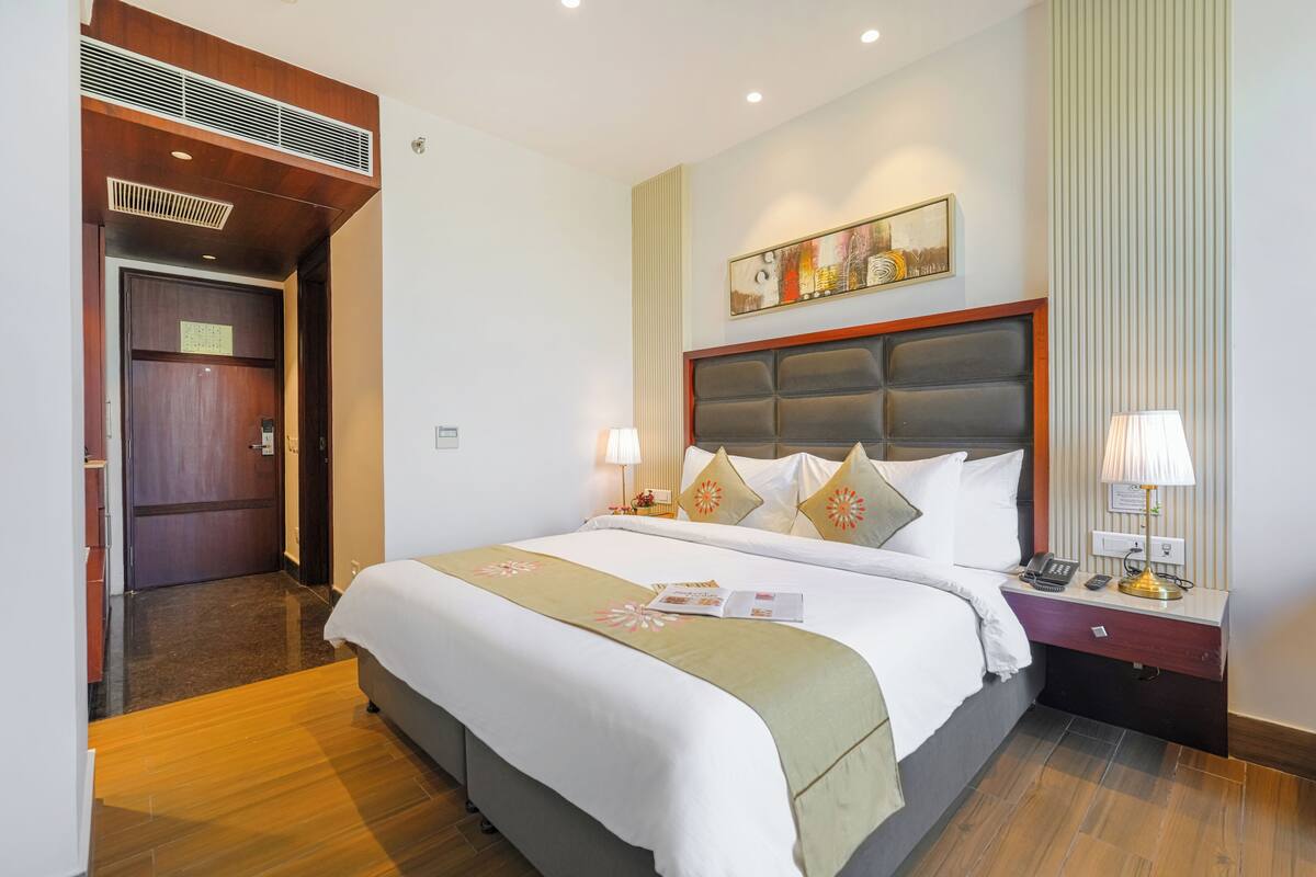 A hotel room with a large bed, bedside tables, a wall-mounted artwork, and a door leading to another room.