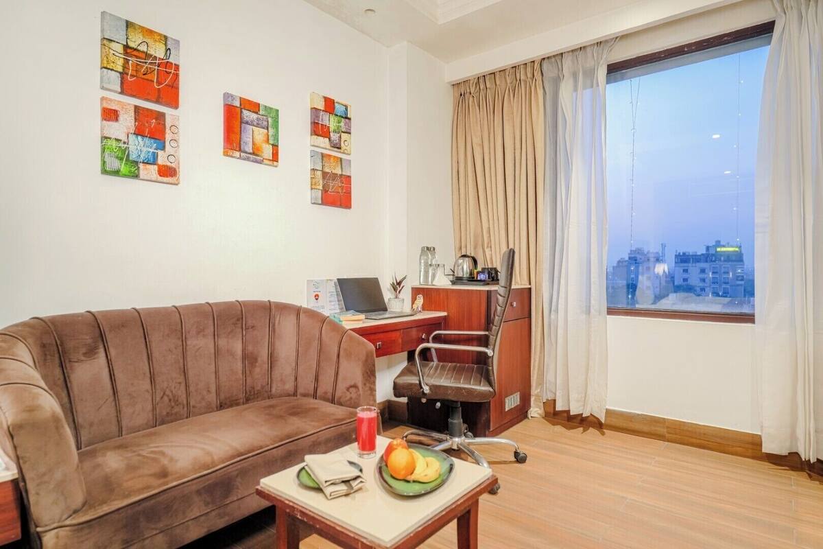 A living room with a brown sofa, a desk with a laptop, a chair, and a window with curtains.
