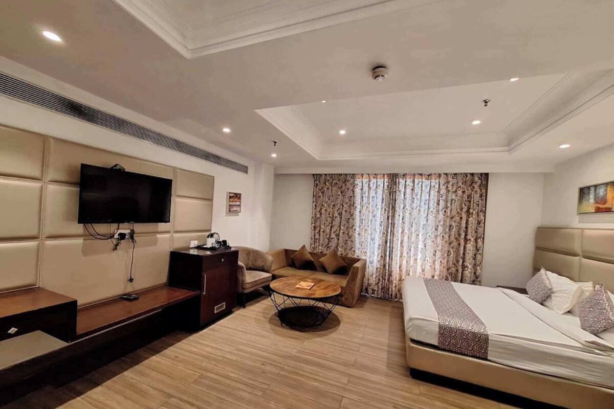A modern hotel room with a flat-screen TV, a sofa, a coffee table, a bed, and a desk.