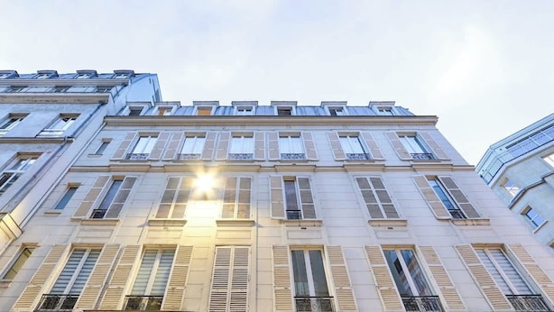 Un edificio de varias plantas con un estilo arquitectónico clásico, que presenta ventanas y contraventanas regularmente espaciadas.