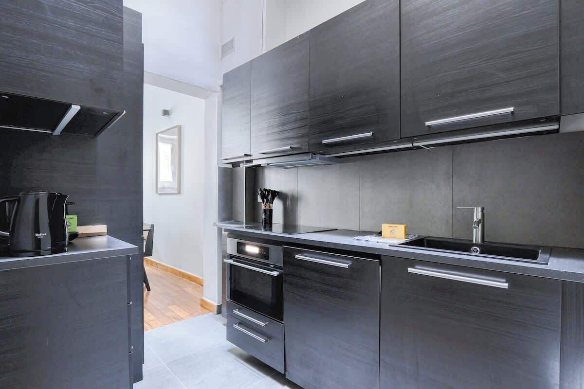 A modern kitchen with dark cabinetry, stainless steel appliances, and a built-in oven.