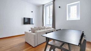 Una sala de estar moderna con un sofá, una mesa de comedor y un televisor montado en la pared.