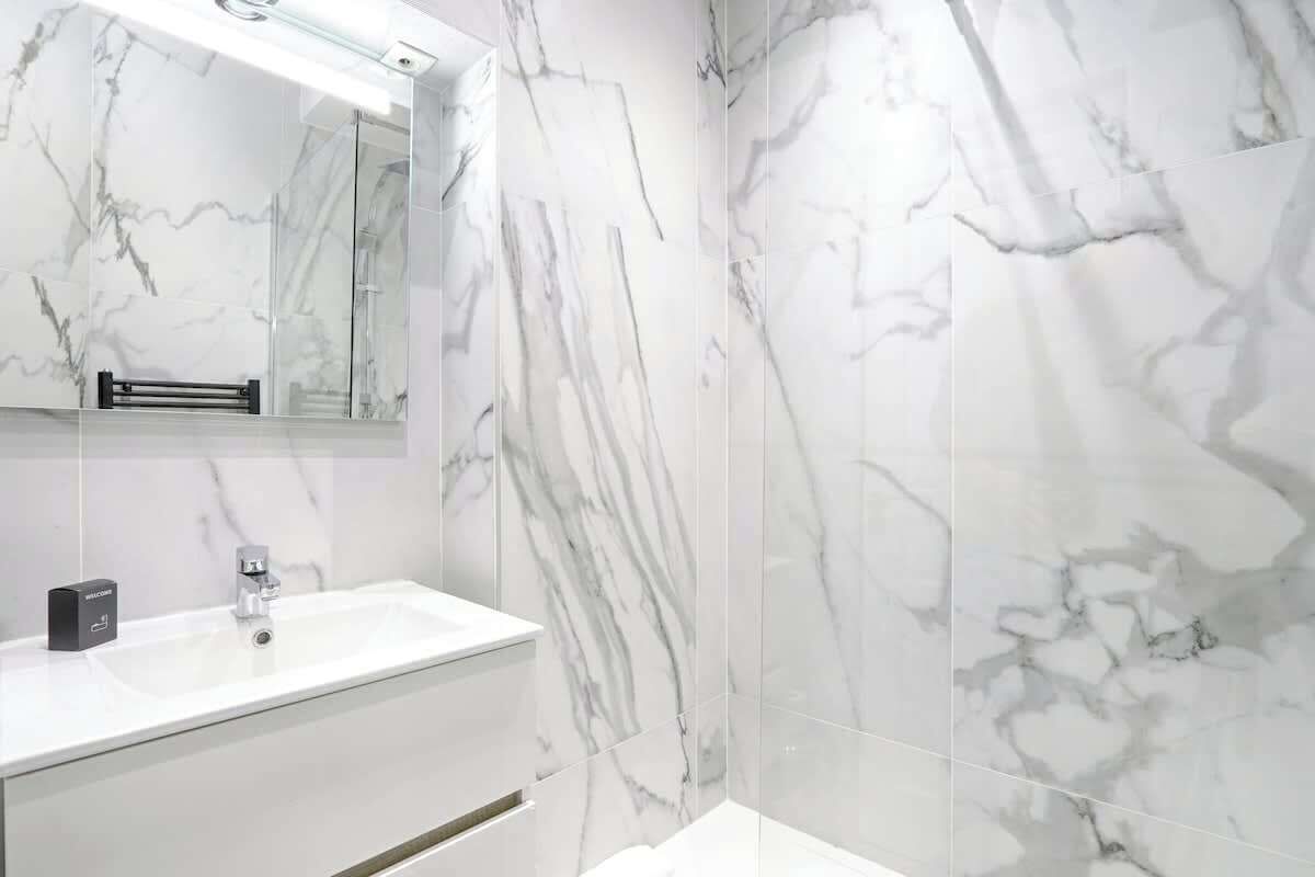 A modern bathroom with a marble backsplash, a white sink, and a mirror above it.