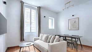 Una sala de estar moderna con un sofá, una mesa de comedor con sillas, una mesita redonda y una ventana con cortinas.