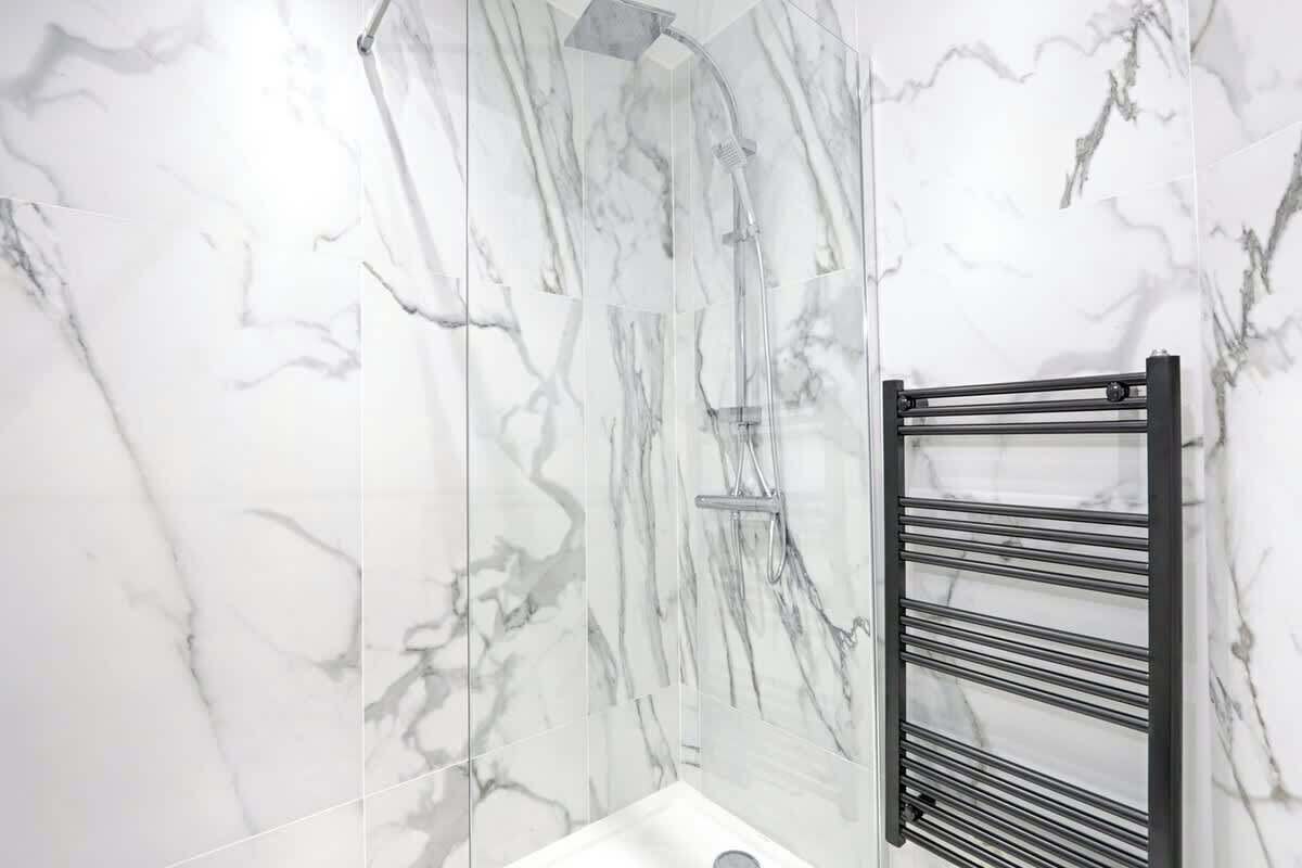 Un baño con paredes de mármol y un perchero negro.