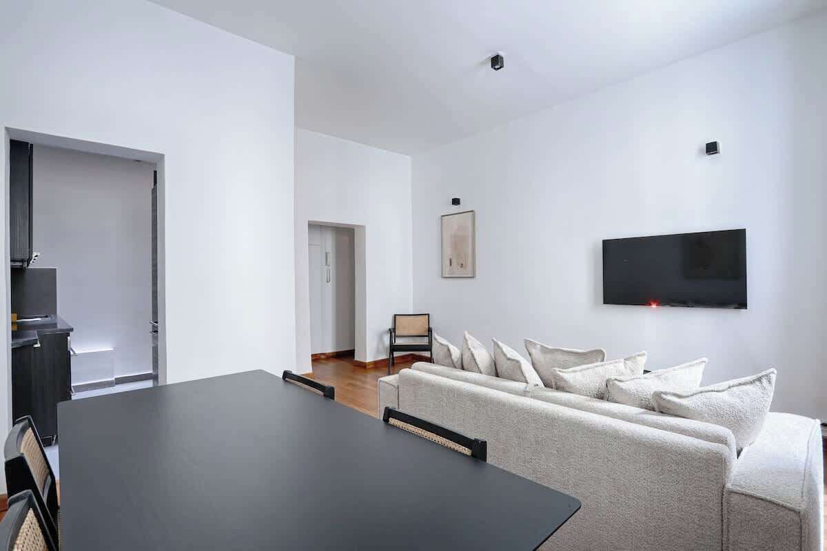 Un salon moderne comprenant une table à manger, un canapé et un téléviseur à écran plat fixé au mur.