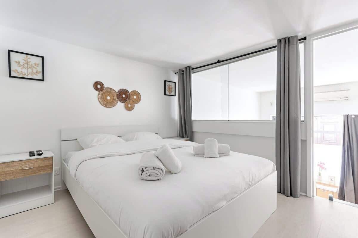 Una habitación de hotel moderna con una cama grande, una mesita de noche y una ventana con cortinas.