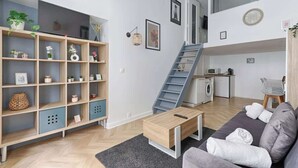En moderne stue med sofa, sofabord og reol. Der er en trappe, som fører op til et niveau med et køkken og en vaskemaskine.