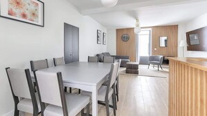 A modern dining area with a white table and chairs, a wooden reception desk, and a living area with a sofa and armchairs. - Batignolles Epinette Lovely Apartment 6P (Paris)