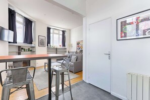 A modern apartment with a kitchen, dining area, and living room. It includes a dining table, chairs, a sofa, and a TV.