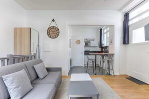 A modern living room with a grey sofa, a small table, and a kitchen in the background.
