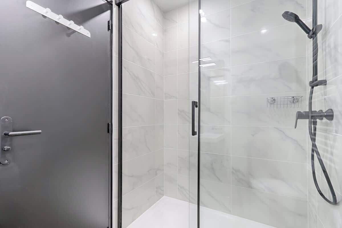 A modern bathroom with a glass shower enclosure, a handheld showerhead, and a towel rack.