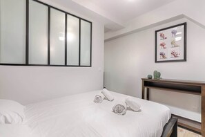 A hotel room with a bed, a nightstand, a framed picture of shoes, and a window with frosted glass panels.