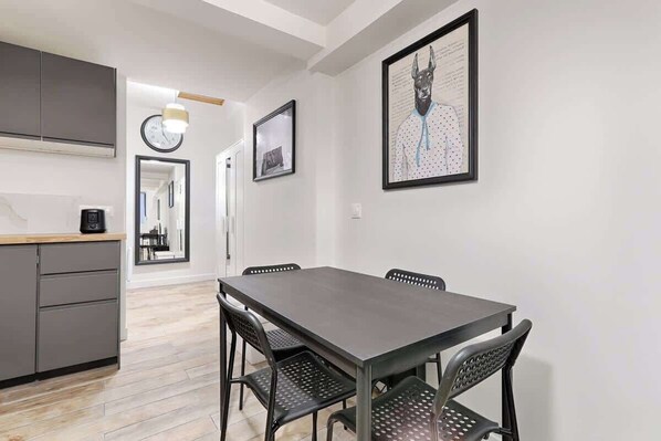 A modern kitchen with grey cabinets, a wooden countertop, and a dining area with a dark table and perforated chairs.