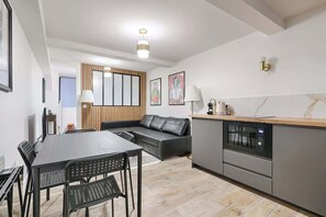 A modern living space with a dining area, sofa, kitchen, and a wooden accent wall.