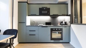 Een kleine keuken met grijze kastjes, een magnetron, een oven en een koffiezetapparaat.