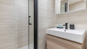 Een moderne badkamer met een douchecabine van glas, een witte wastafel met een zwarte kraan en een spiegel boven de wastafel.