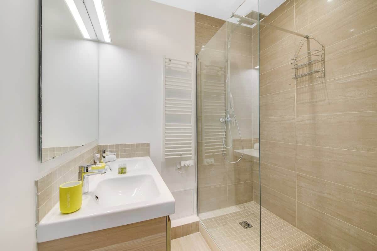 A modern bathroom with a glass shower enclosure, a white sink, and a yellow cup on the counter.
