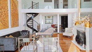 Uma sala de estar ampla, com uma escada moderna, lareira e uma grande obra de arte na parede.