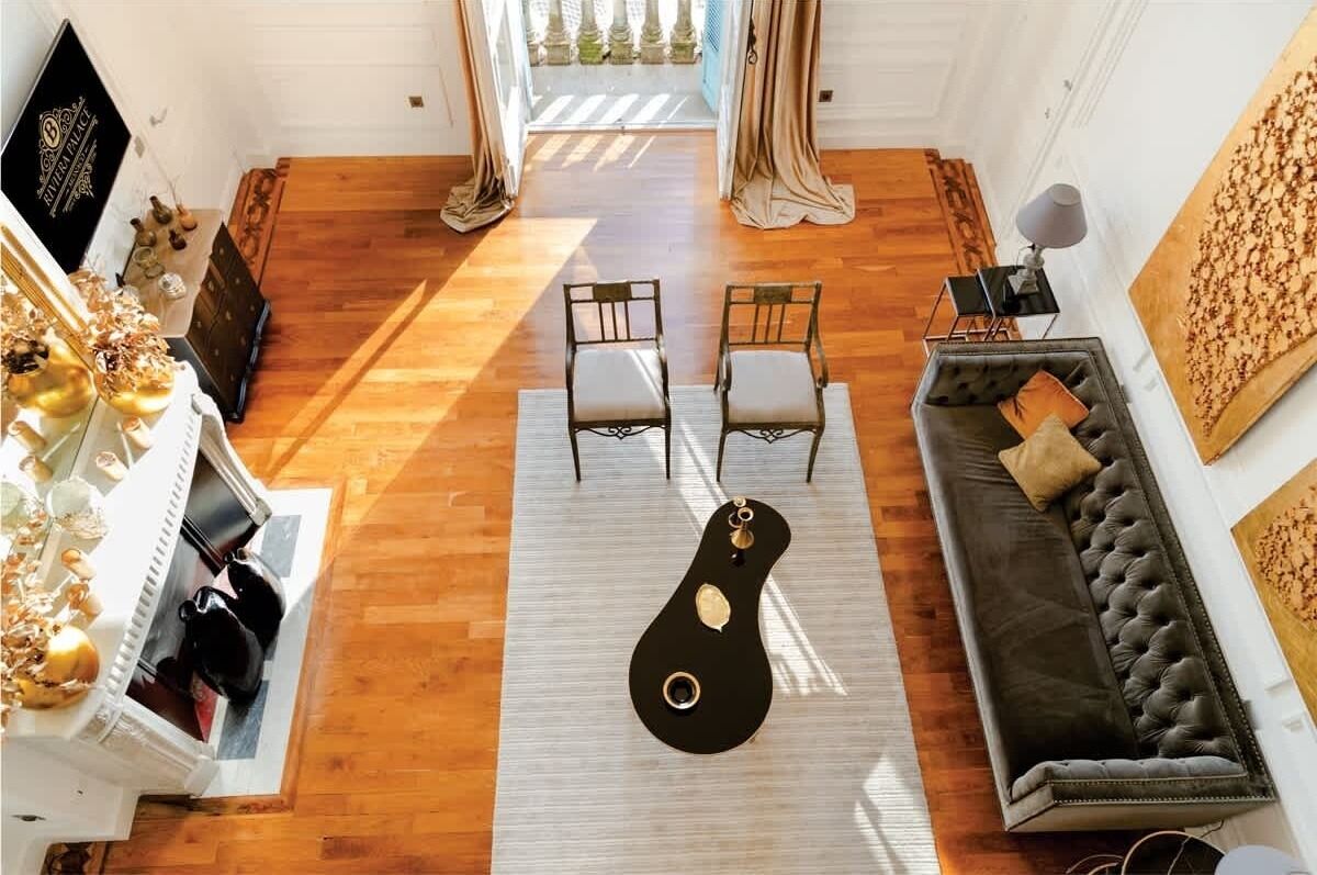 Un salon spacieux doté d’un plancher en bois, d’une table basse noire, de deux fauteuils, d’un canapé et d’une grande fenêtre avec des rideaux.
