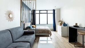 Un soggiorno moderno con un divano grigio, un letto con testiera decorata e un'area da pranzo con uno sgabello da bar.