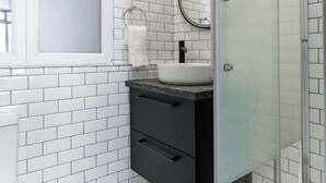 Un bagno moderno con piastrelle bianche tipo metro, box doccia in vetro, specchio rotondo e mobile lavabo nero.