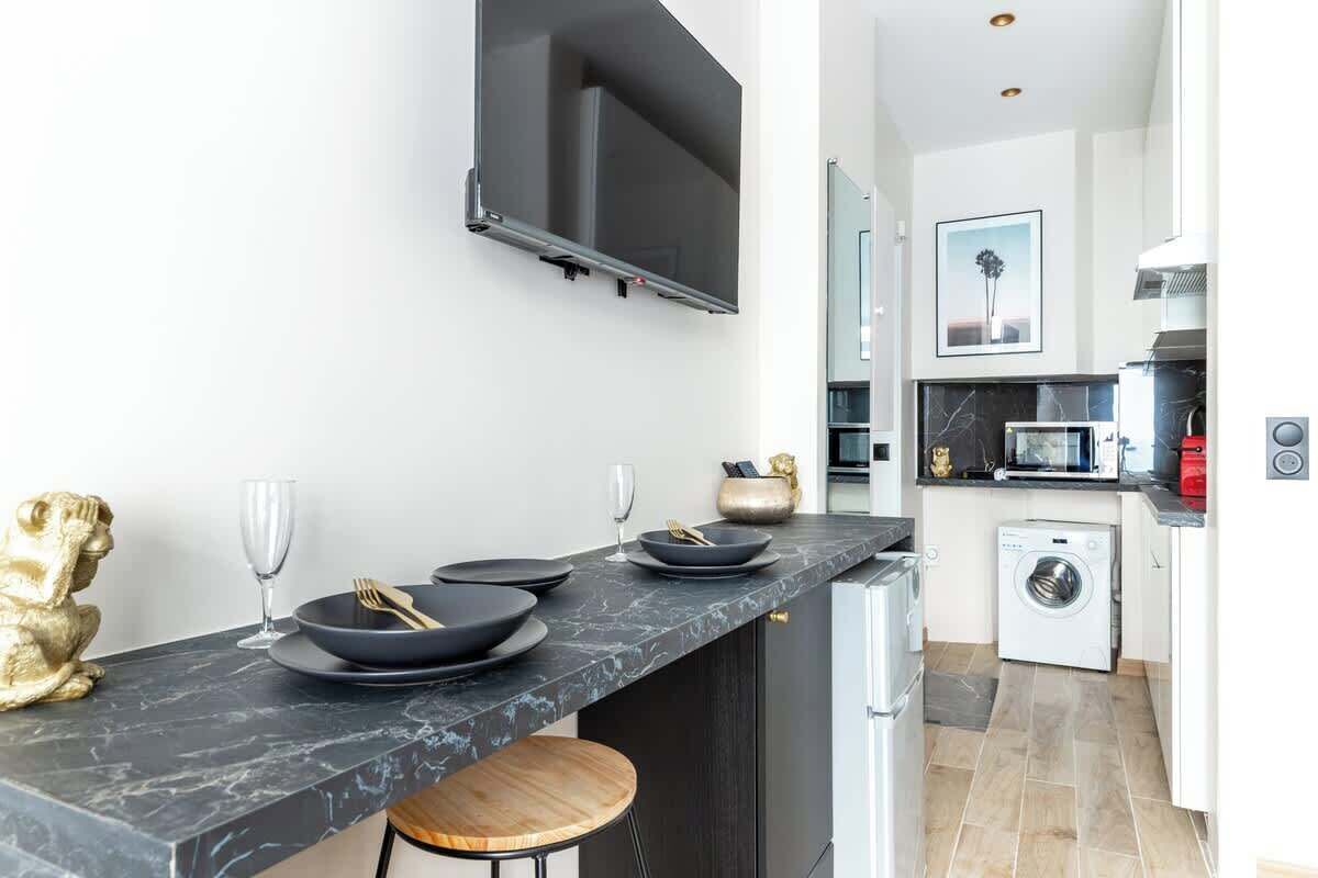 A modern kitchen with a marble countertop, a flat-screen TV, a washing machine, and a microwave.