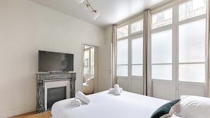 Una habitación de hotel con una cama grande, chimenea, televisor y ventanas amplias.