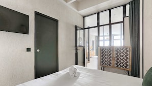 Ein Hotelzimmer mit einem Bett, einer dunklen Tür, einem großen Fenster mit Vorhängen und einer verzierten Innentür.