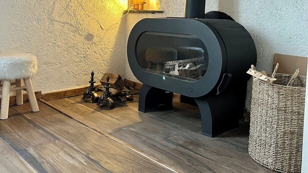 A modern fireplace with a glass front, a wooden stool, and a woven basket.