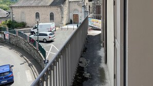 A balcony overlooking a street with a historic building, a mountain backdrop, and a clear sky.