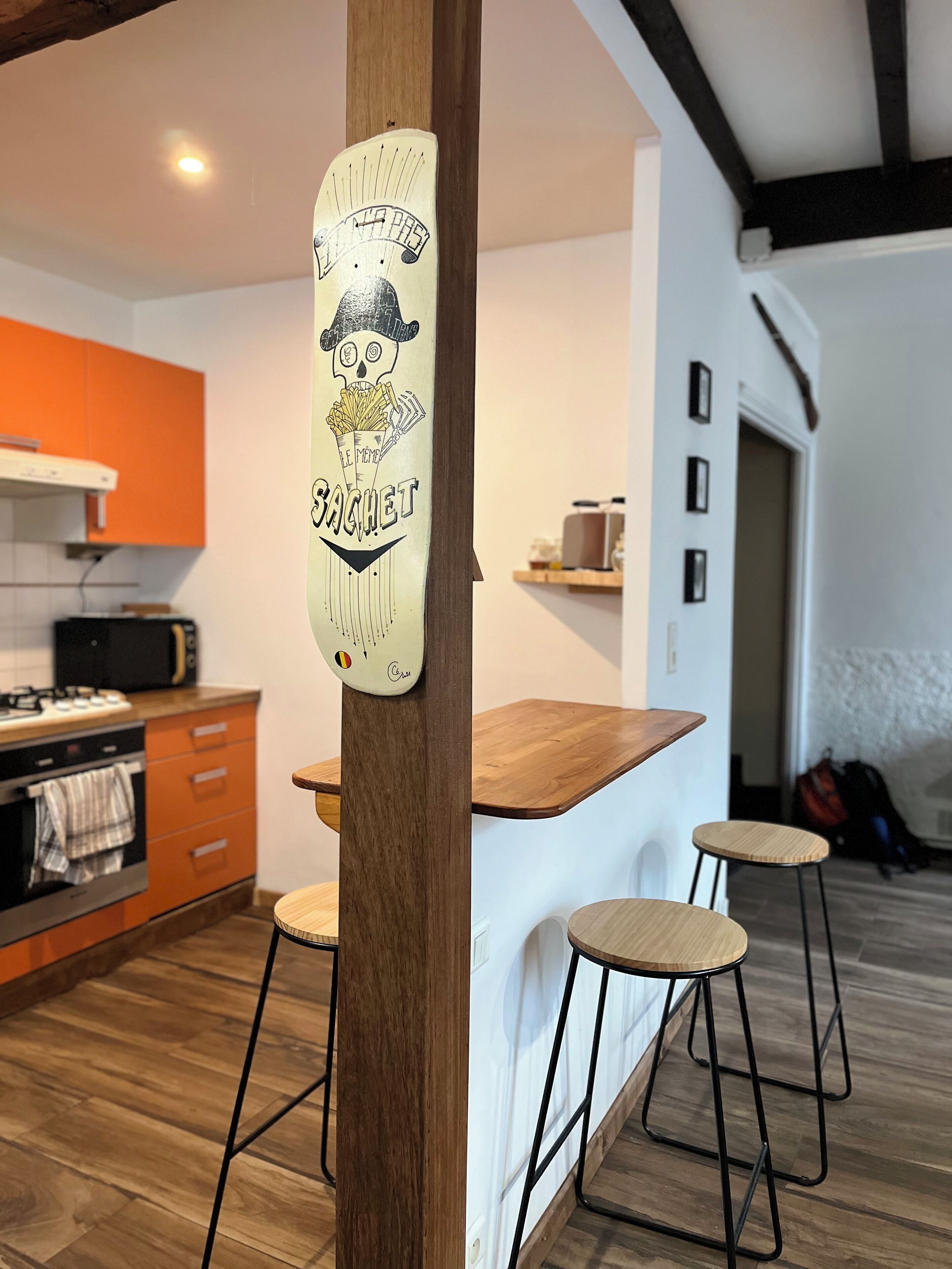A kitchen area with a wooden bar counter, two stools, and a wall-mounted sign with a graphic and text.