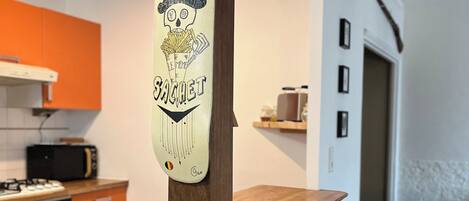 A kitchen area with a wooden bar counter, two stools, and a wall-mounted sign with a graphic and text.