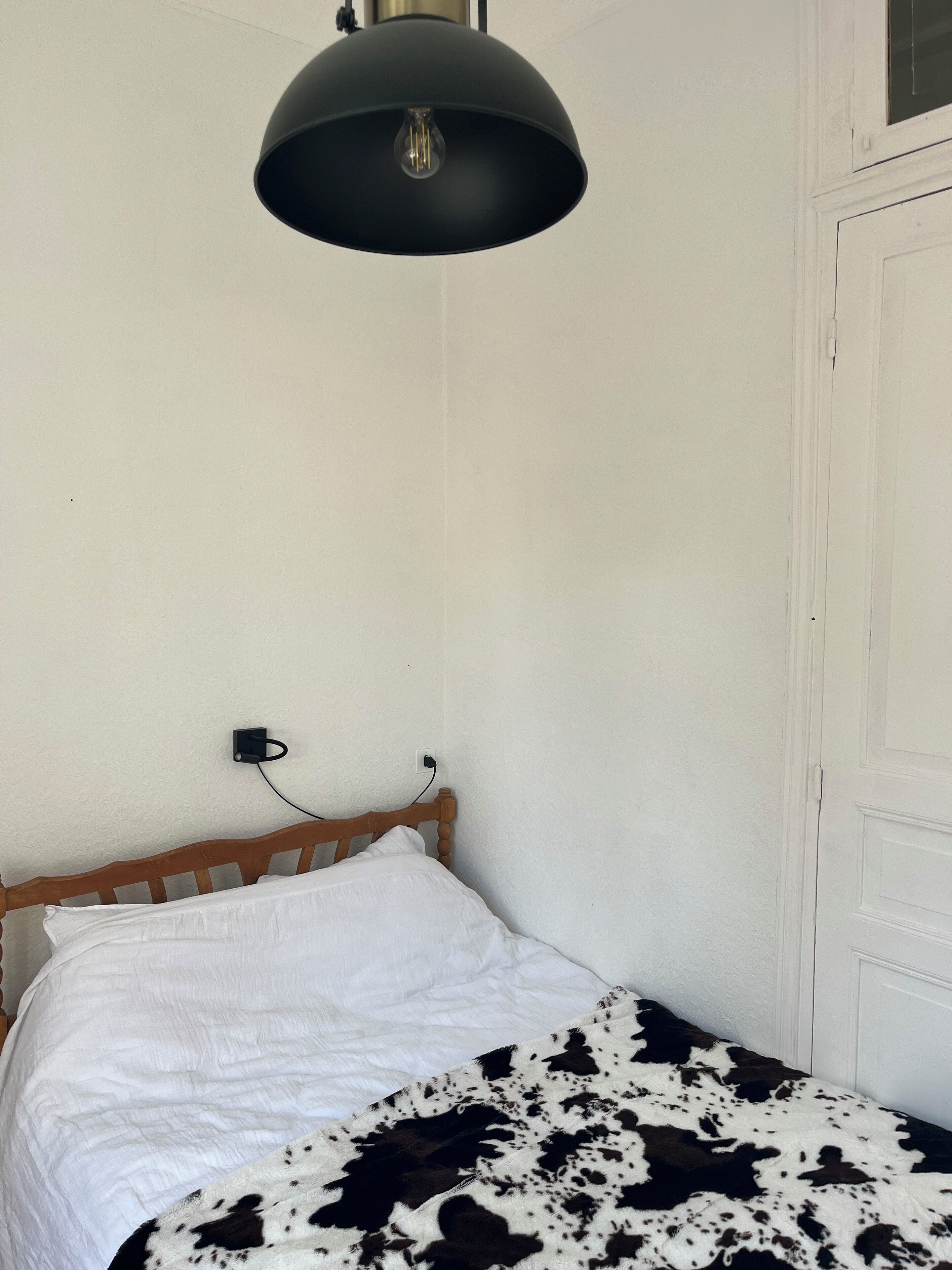 A bedroom with a bed, a wooden headboard, a black pendant light, and a white door.
