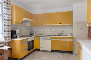 Une cuisine avec des meubles de couleur jaune, un plan de travail blanc, une machine à café, un lave-vaisselle et une cuisinière.