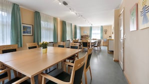 Ein geräumiger Essbereich mit einem langen Holztisch und Stühlen, einer kleinen Pflanze auf dem Tisch sowie einer Küche im Hintergrund.