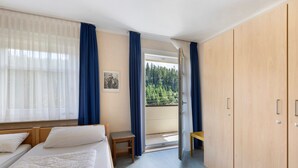 Ein Hotelzimmer mit Bett, Stuhl, Holzschrank und einem Balkon mit Blick auf Bäume.
