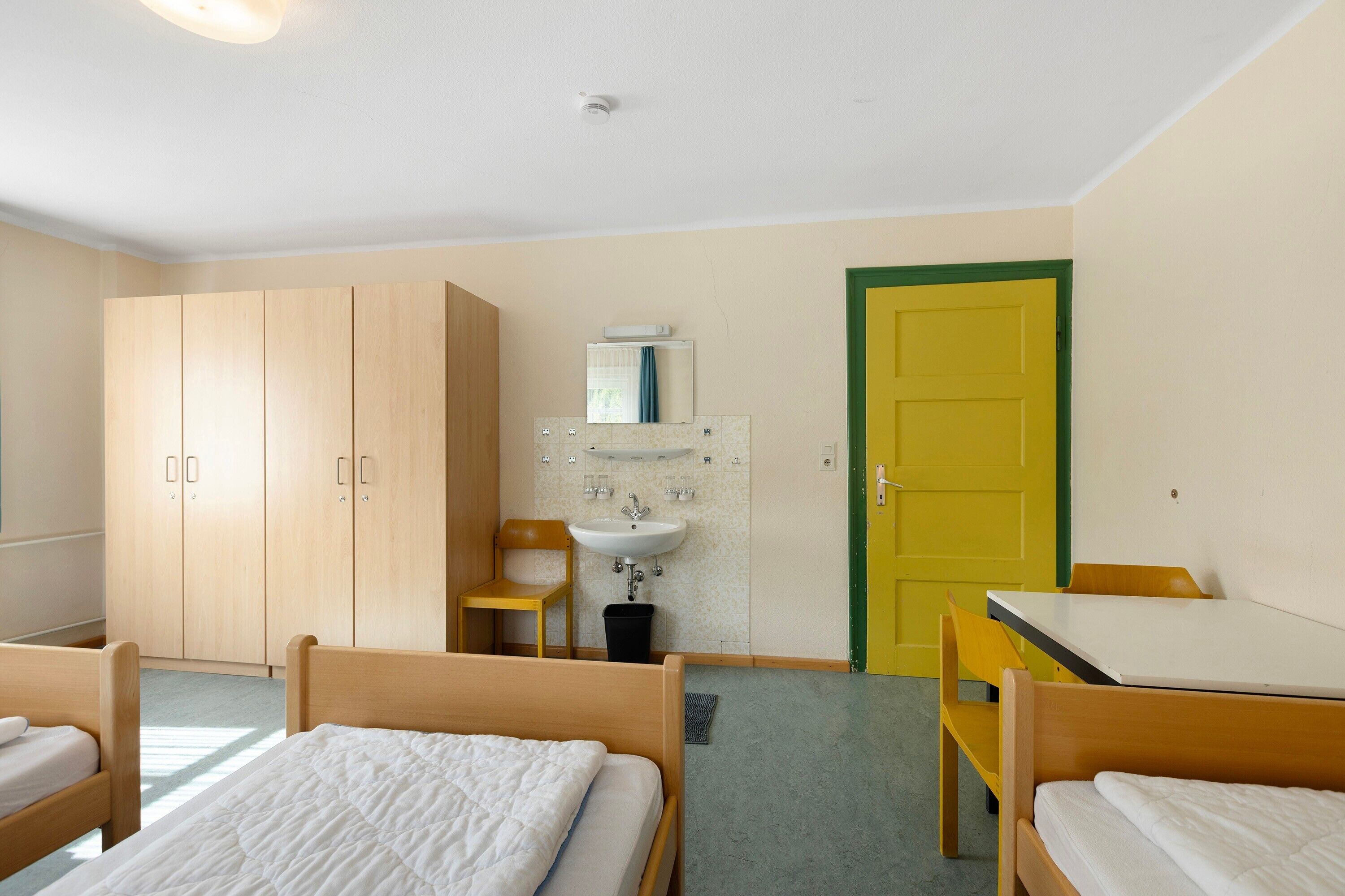 A room with two beds, a sink, a mirror, and a yellow door.
