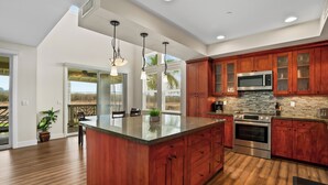 Una cocina moderna con armarios de madera, una isla grande, electrodomésticos de acero inoxidable y vistas al exterior.