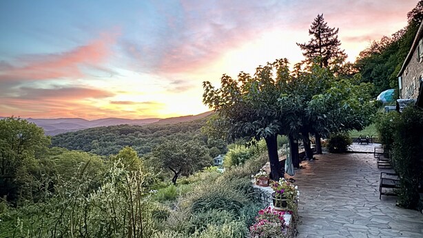 A stone pathway leading to a building with a view of a forested hillside and a sunset. - Bella Dome - Cosy dome with panoramic mountain views, surrounded by beautiful nature (Riols)