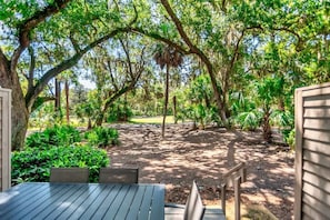 An outdoor patio area with a table and chairs, surrounded by lush greenery and trees.