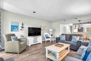 A living room with a TV, sofa, coffee table, and a dining area with chairs.