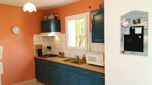 Une cuisine avec des meubles bleus, un micro-ondes blanc et une fenêtre donnant sur des arbres.