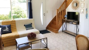 Un salon avec un canapé, une table basse et un téléviseur posé sur un bureau. Un escalier mène à un autre niveau.