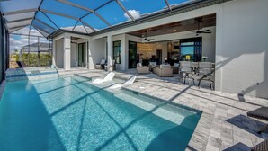 Un espace piscine extérieur moderne, doté d’une structure en verre, de chaises longues et d’un coin repas avec des sièges en plein air.